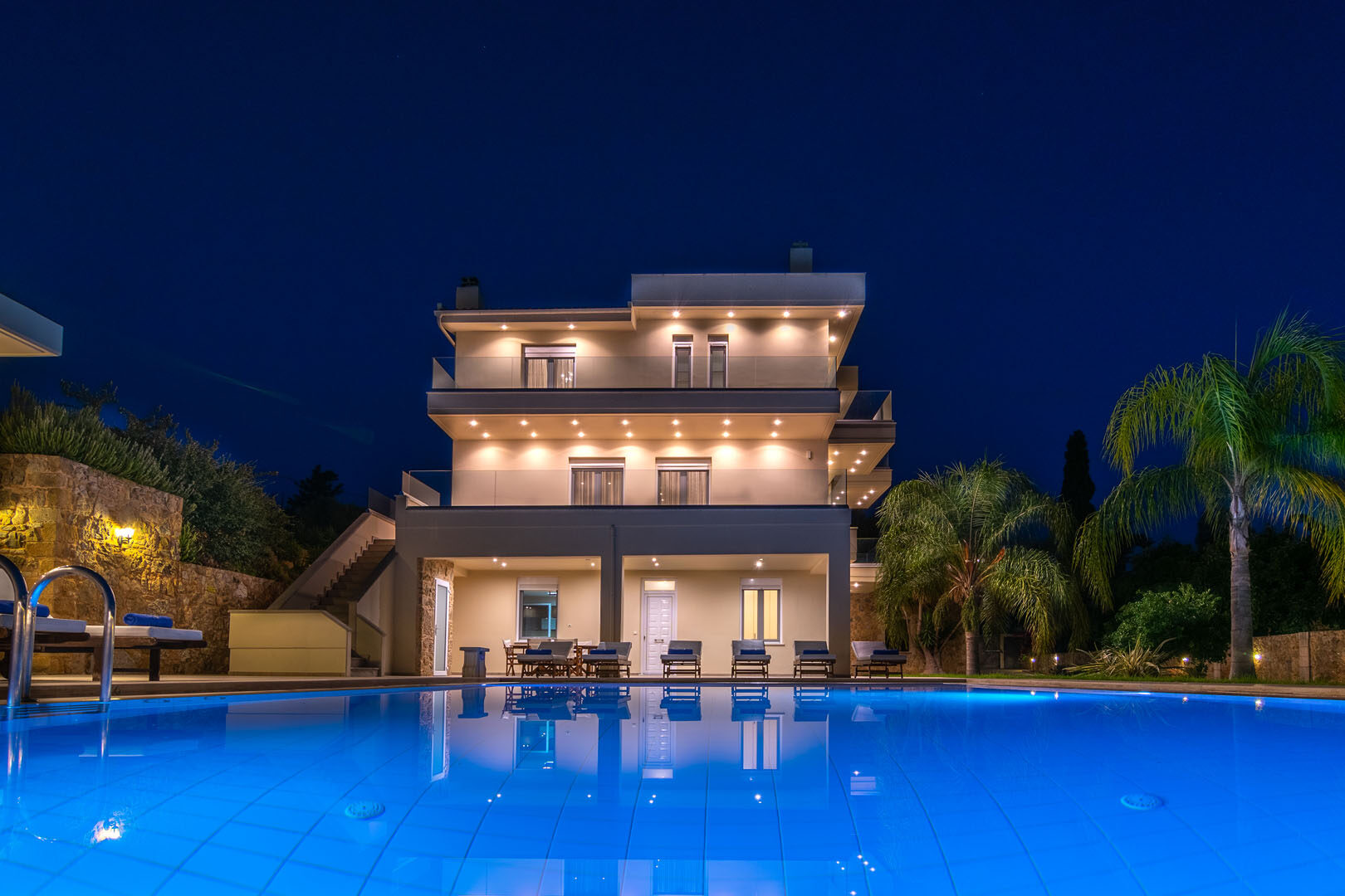 Villa Melitini at night — the illuminated three-level villa reflected in its glowing blue pool